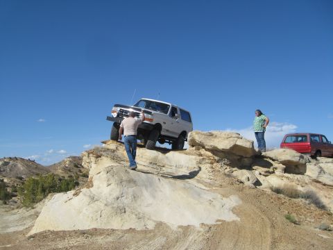 1993 Ford Bronco - A white Ford Bronco is parked on a rocky incline with a person standing next to it. A red SUV is parked further back on the right.