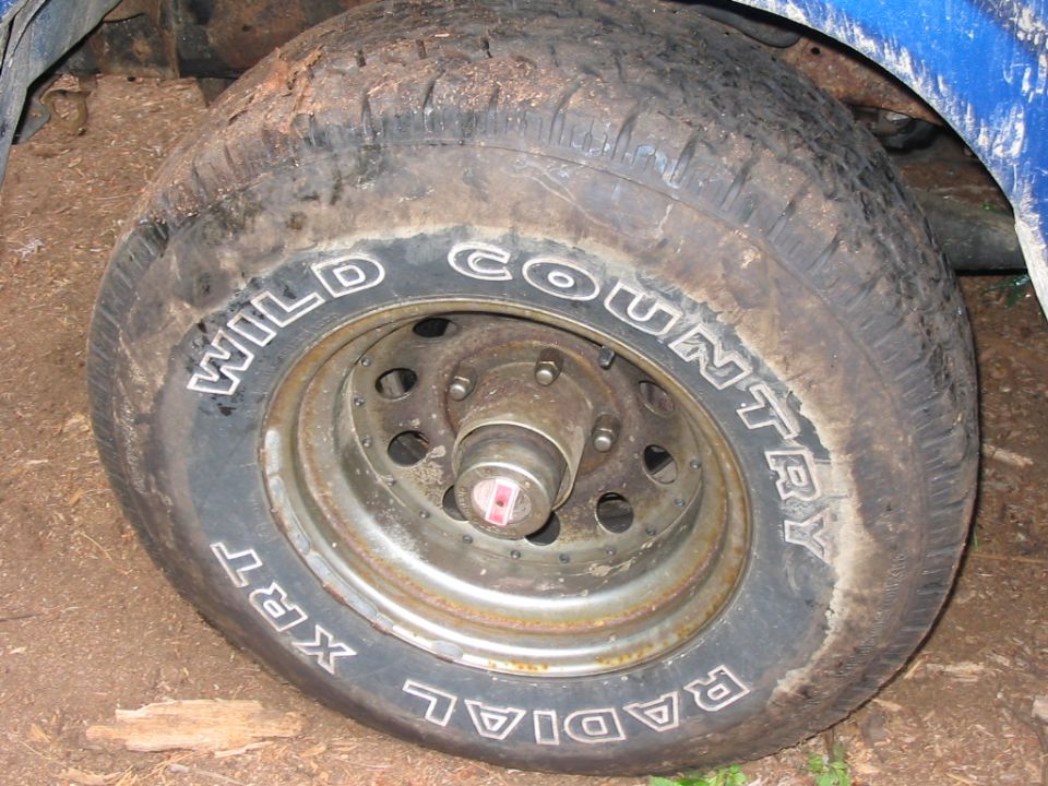 Mud-covered tire with white lettering 'WILD COUNTRY XRT RADIAL' on a rusty wheel