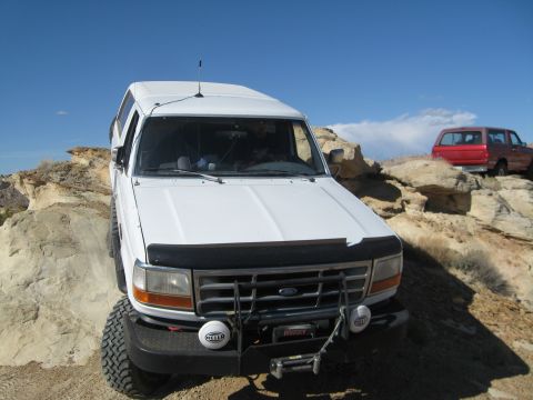 1993 Ford Bronco - A white Ford Bronco is parked on a rocky incline with a red Ford Bronco visible in the background. The white Bronco is facing the camera an…