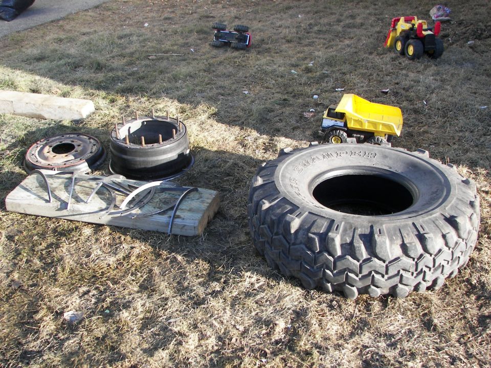 Toy dump truck and construction toys on grass with large tire and wheel parts