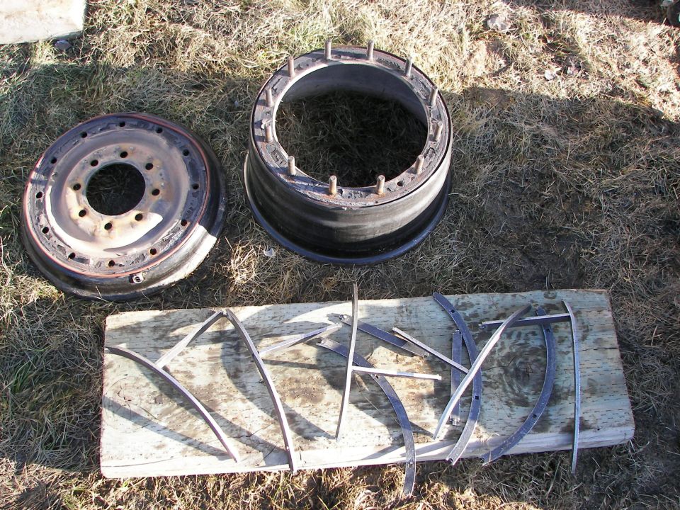 Two vehicle wheel rims and some metal strips laid out on a wooden board