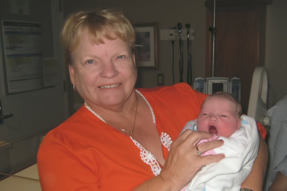 Woman in orange shirt holding a newborn baby, hospital room background with medical equipment