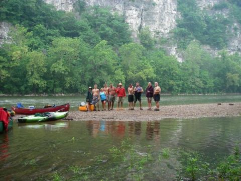 1978 Ford Bronco - A group of people gather on a riverbank with canoes and kayaks, with a rocky cliff face in the background.