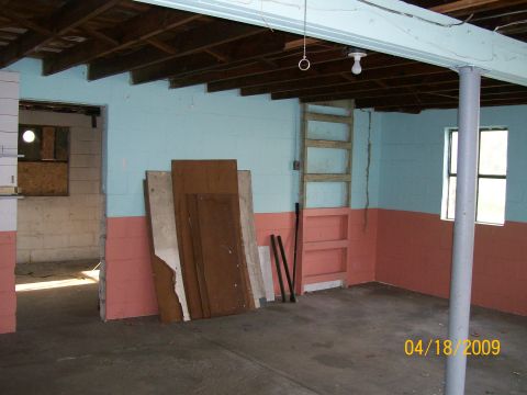 1995 Mercury Grand Marquis - Empty interior of a cinder-block garage or basement painted pale blue above and salmon pink below, with a bare concrete floor, exposed floo…