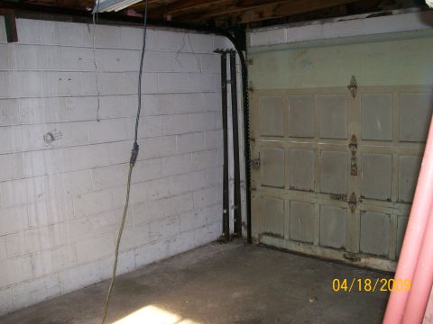 1995 Mercury Grand Marquis - Corner of an empty single-bay garage with whitewashed cinder-block walls, a bare concrete floor and an old paneled wood overhead door with…