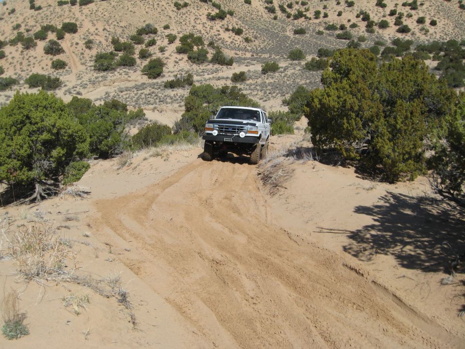 White Ford Bronco climbing a sandy hill, front view, with aftermarket bumper and lights