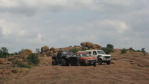 1979 Ford Bronco - Three off-road vehicles are parked on a rocky hillside under a cloudy sky.