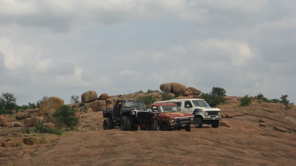Off-road vehicles parked on rocky hill: black pickup, red pickup, and white van