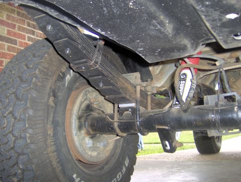 1995 Ford Bronco - Close-up view of the rear suspension and axle of a vehicle, showing leaf springs and a shock absorber.