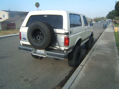 1988 Ford Bronco - Rear view of a lifted white Ford Bronco with a spare tire mounted on the tailgate.