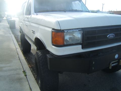 1988 Ford Bronco - A white Ford Bronco is parked on the side of the road, showing its front end and lifted suspension.
