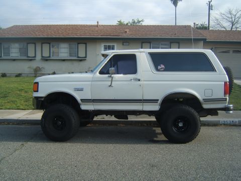 1988 Ford Bronco - This lifted SUV is parked on a residential street in front of a house.