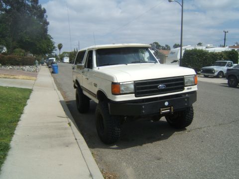 1988 Ford Bronco - This lifted Ford Bronco sits parked on a residential street with a sidewalk and grass verge.