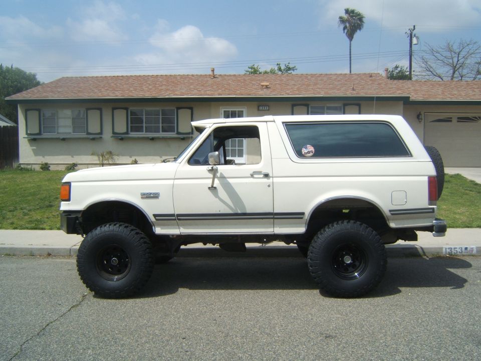 White Ford Bronco with lifted suspension and large tires parked on a residential street