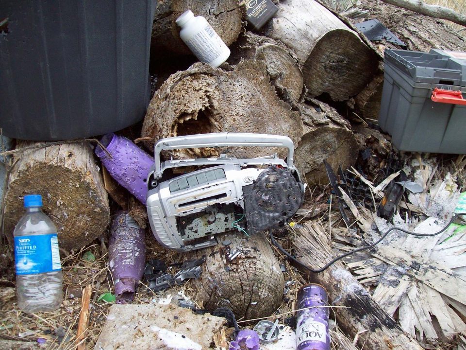 Broken silver boombox, purple bottles, and a water bottle among logs and debris