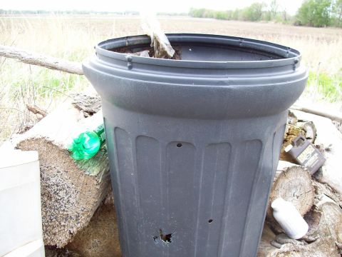 2000 Mercury Grand Marquis - A close-up view of a large, damaged trash can filled with dirt and debris, with a rural landscape in the background.