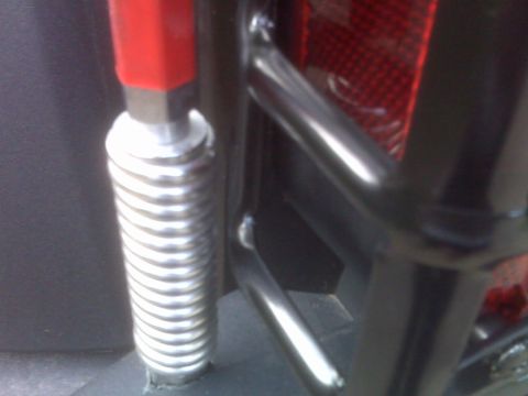 2008 Jeep Wrangler - Close-up view of a vehicle's rear tail lamp guard and a silver shock absorber with a red top.