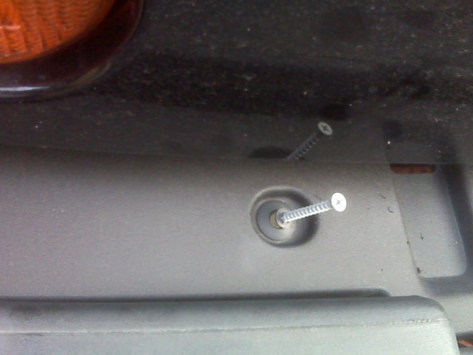 Two screws inserted into gray plastic trim with orange light visible at top left