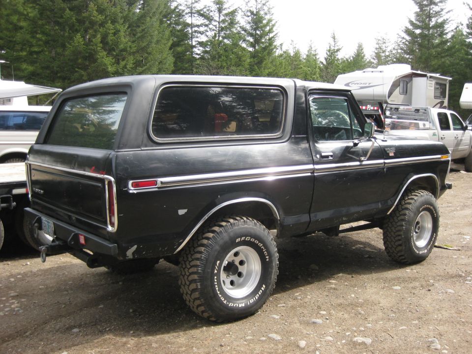 Black Ford Bronco parked on dirt lot, trees and RVs in background