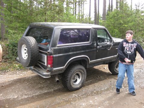 1979 Ford Bronco - This black 1979 Ford Bronco is seen from the rear three-quarter angle, parked on a dirt road.