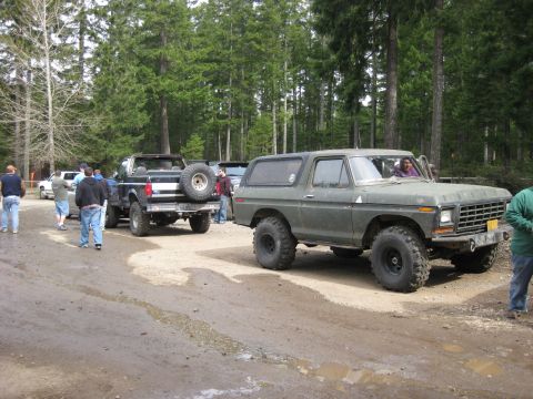 1979 Ford Bronco - A group of people and several off-road vehicles are gathered on a dirt road in a wooded area.