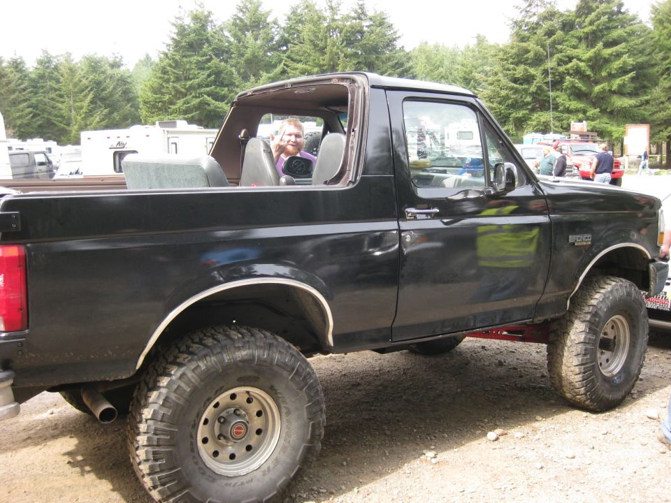 Black SUV with a person in the driver's seat, lifted suspension, off-road tires, and a removable top