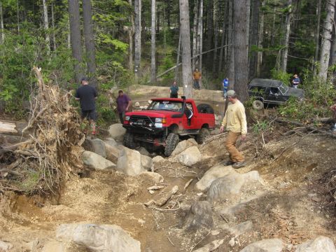 1979 Ford Bronco - Off-road vehicles tackle a challenging, boulder-strewn path in a wooded area.