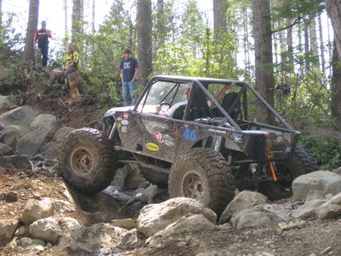 1979 Ford Bronco - A heavily modified off-road buggy tackles a challenging rocky terrain in a wooded area.