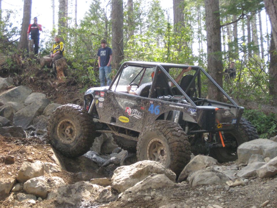 Mud-covered off-road buggy with a roll cage navigating a rocky trail