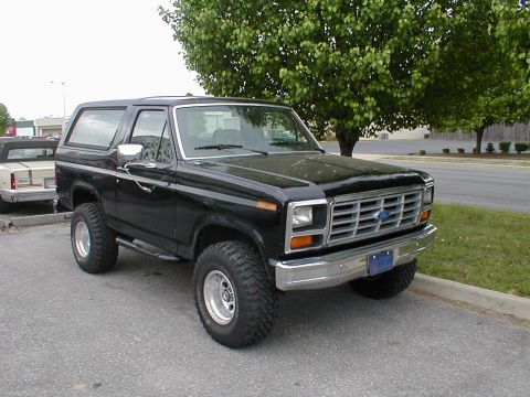 1983 Ford Bronco - This black Ford Bronco is parked on a street with a tree in the background.
