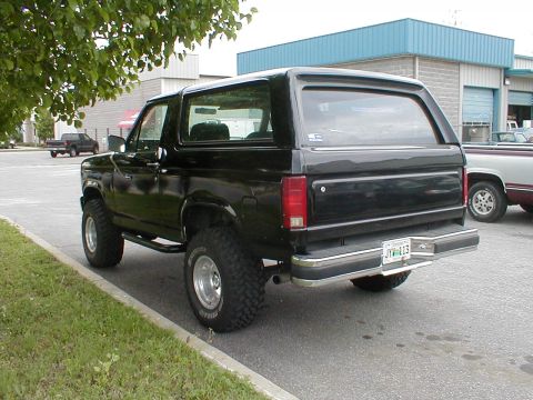 1983 Ford Bronco - Rear view of a black SUV with tinted windows and chrome accents parked next to a building.