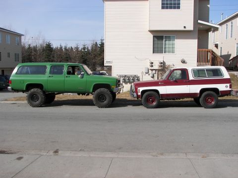 1990 Chevrolet Suburban - Two classic Chevrolet SUVs, a Suburban and a K5 Blazer, are parked on a street.