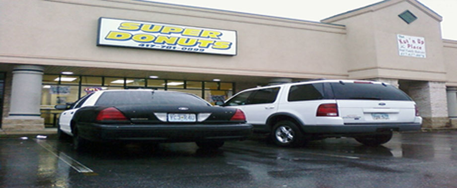 Black and white police car and white SUV parked in front of Super Donuts