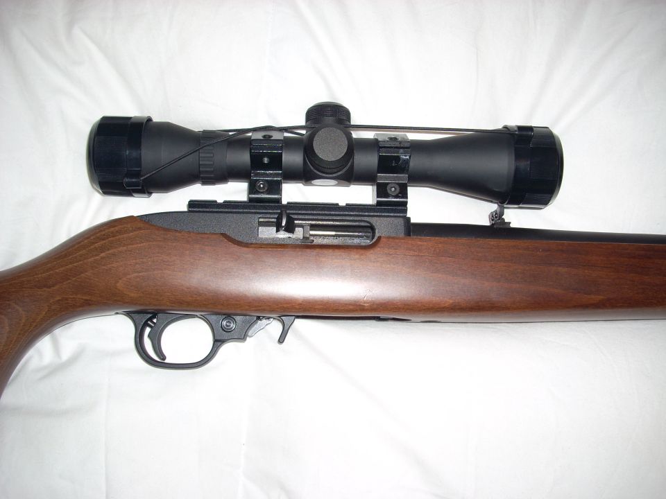 Close-up of a wood-stocked rifle receiver and mounted black scope on white bedding