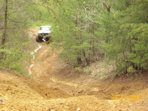 1978 Ford Bronco - A 1978 Ford Bronco navigates a challenging muddy incline in a wooded area.