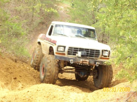 1978 Ford Bronco - This heavily modified truck navigates a steep, muddy incline, its off-road capabilities.