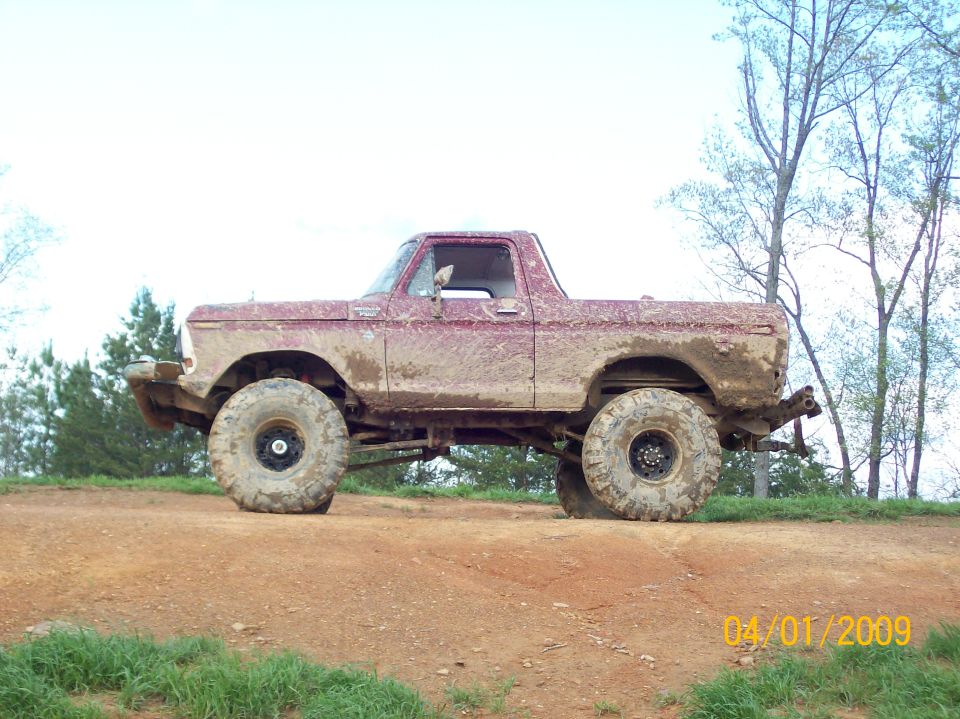 Topless lifted red Ford Bronco caked in mud, side view on a red clay hilltop