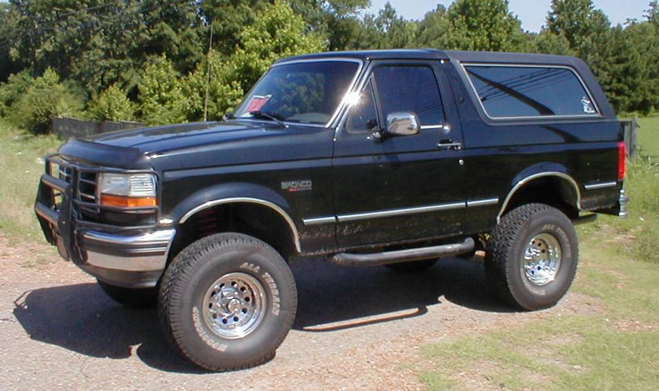 Black lifted Ford Bronco SUV on chrome wheels, front 3/4 view on gravel