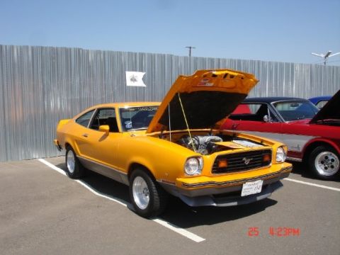 1978 Ford Mustang II - A yellow 1974 Ford Mustang II coupe is parked next to a red car, with its hood open.