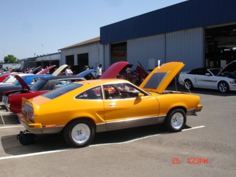 1978 Ford Mustang II - An orange 1978 Ford Mustang II hatchback is displayed with its hood open at an outdoor car show, alongside other vehicles.