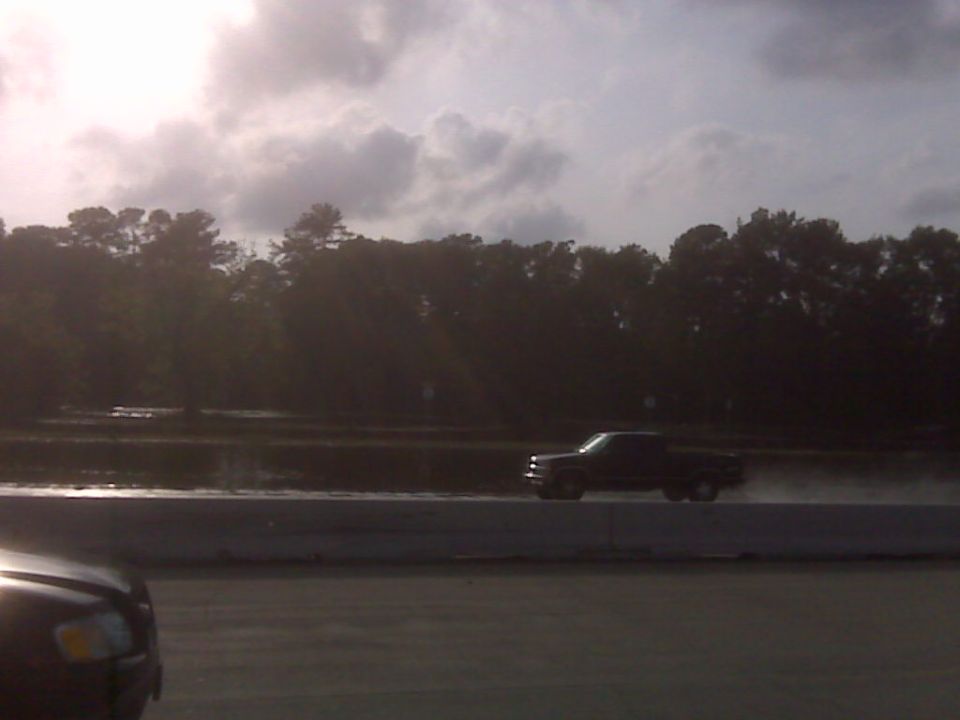 Dark pickup truck driving on a wet surface with trees in the background
