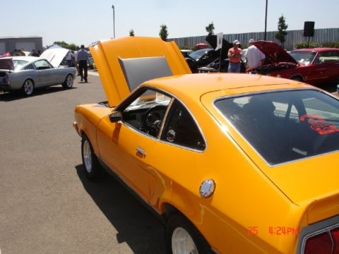 1978 Ford Mustang II - A bright orange coupe is parked at an outdoor car show with its hood open.
