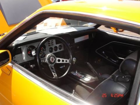 1978 Ford Mustang II - The interior of a yellow 1978 Ford Mustang II shows black seats, a dashboard with gauges, and a four-spoke steering wheel.