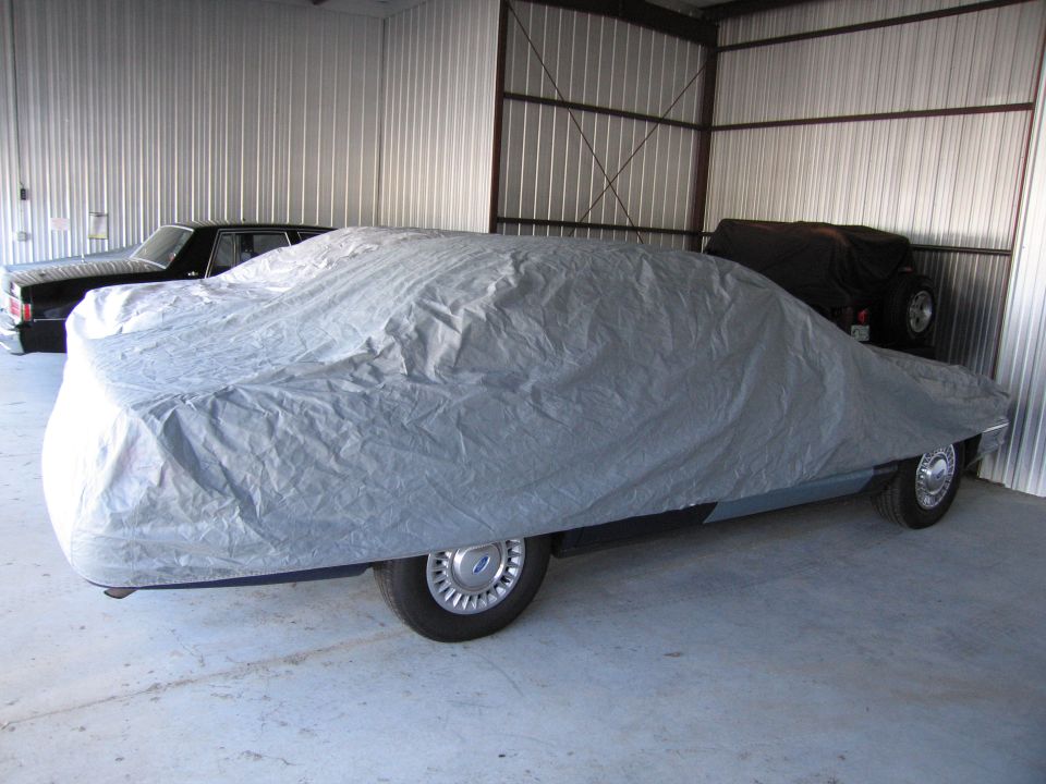 Car covered by a gray tarp, parked next to a black car and a Jeep in a storage unit