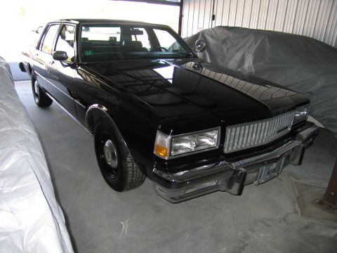1991 Ford LTD Crown Victoria - A black sedan, possibly from the early 1990s, is parked in a garage with other covered vehicles.
