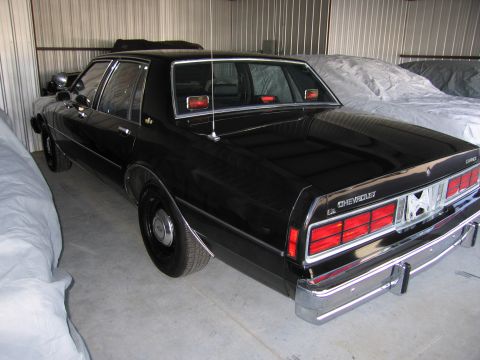 1991 Ford LTD Crown Victoria - Rear view of a black Chevrolet Caprice sedan parked indoors, showing its taillights and chrome bumper.