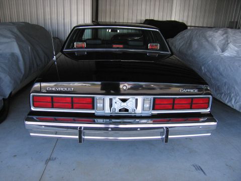 1991 Ford LTD Crown Victoria - The rear of a black Chevrolet Caprice is visible, parked next to a covered vehicle in a garage.