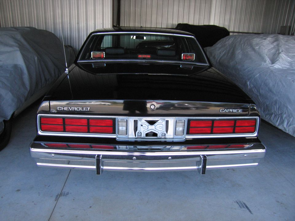 Black Chevrolet Caprice parked in a garage, rear view. Another car covered with a tarp is to the left