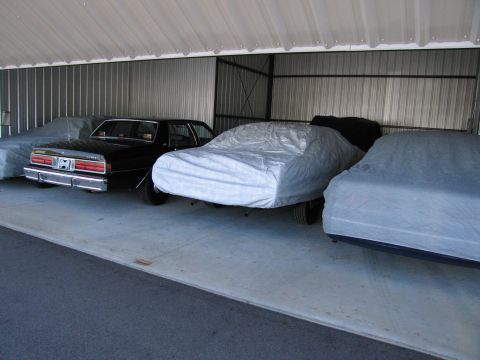 1991 Ford LTD Crown Victoria - A black sedan is parked in a storage unit alongside other vehicles covered with car covers.