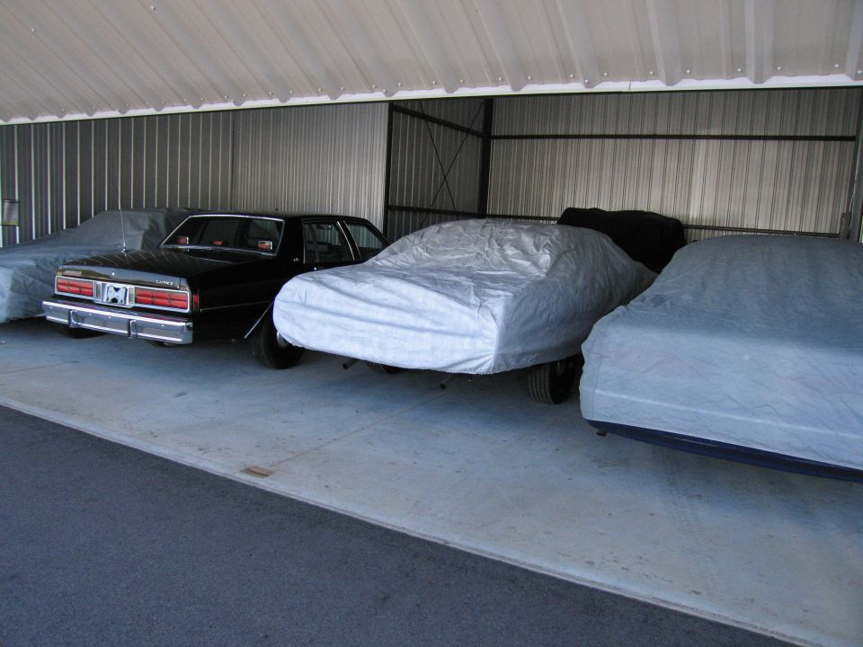 Black sedan with chrome bumper and rectangular taillights, parked inside a metal storage unit